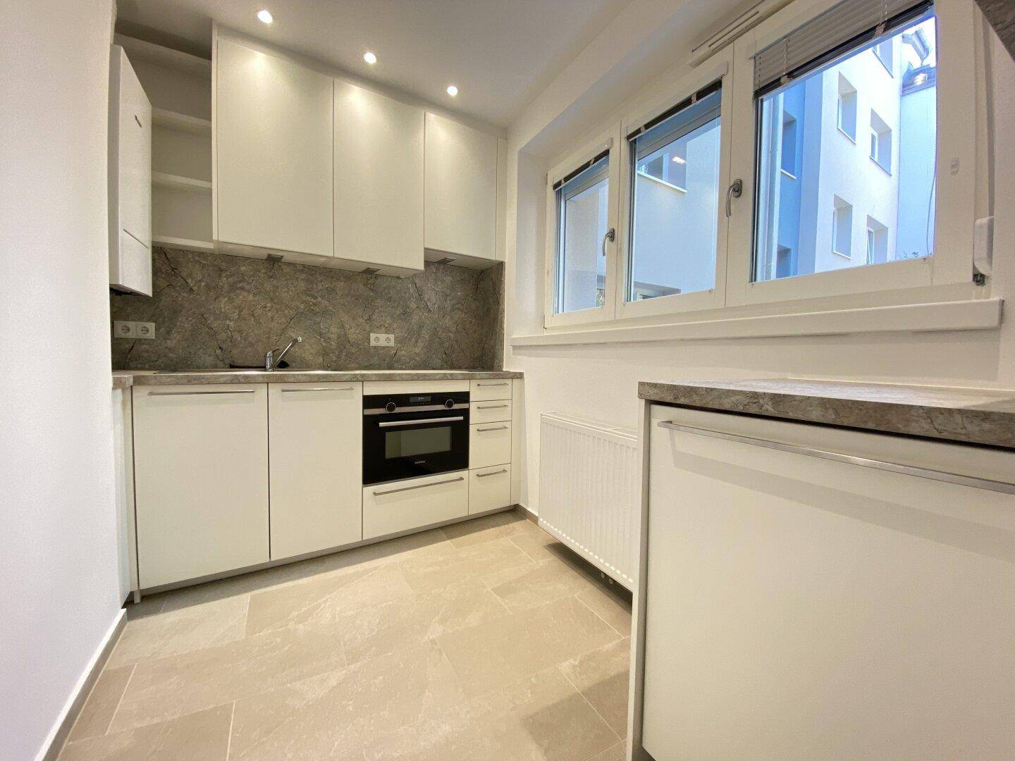 Moderne Einbauküche mit weißen Schränken, integrierten Geräten und Fensterblick.
