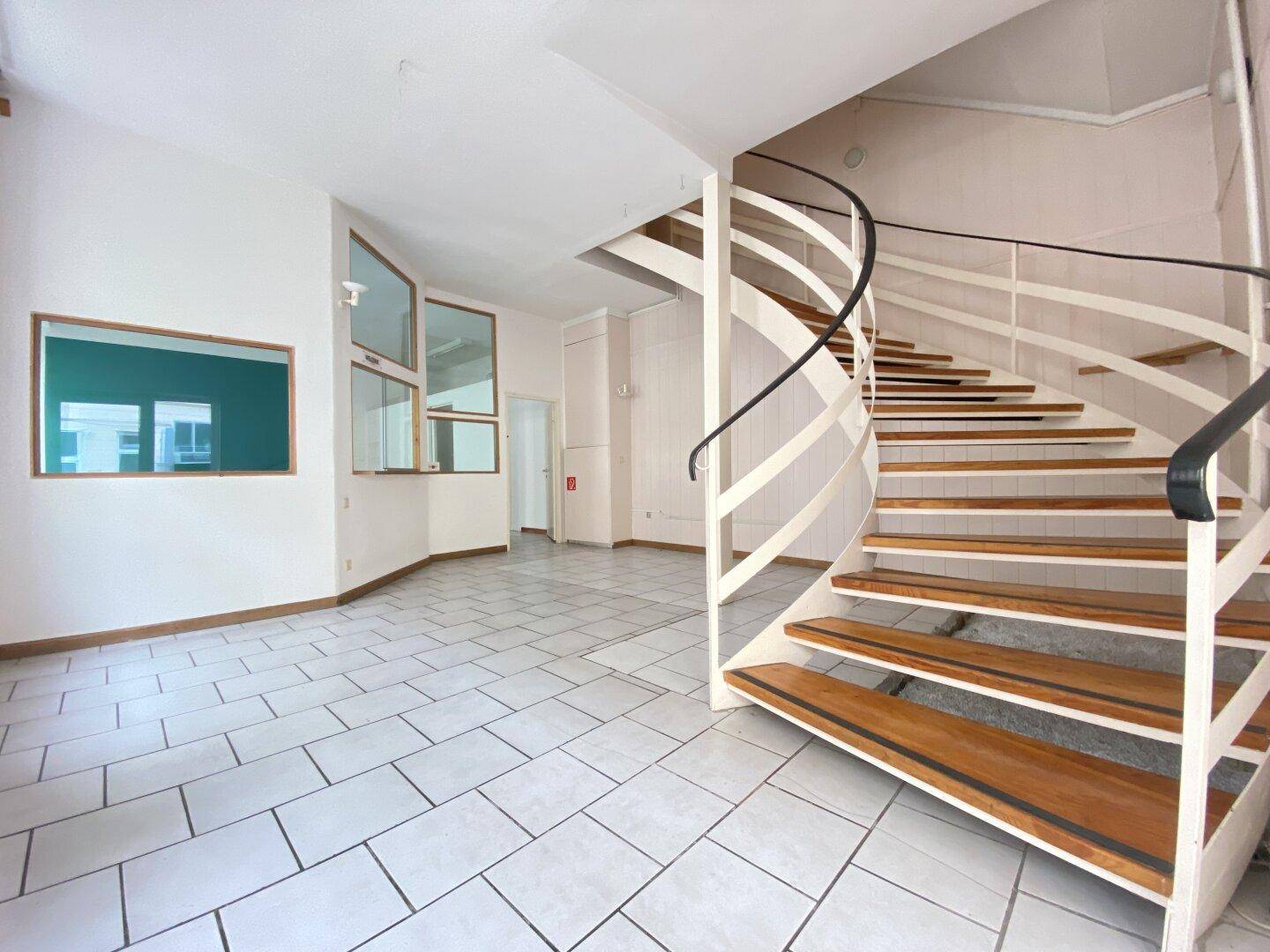 Heller Eingangsbereich mit weißem Fliesenboden und einer markanten Holz-Wendeltreppe, die in die obere Etage führt.