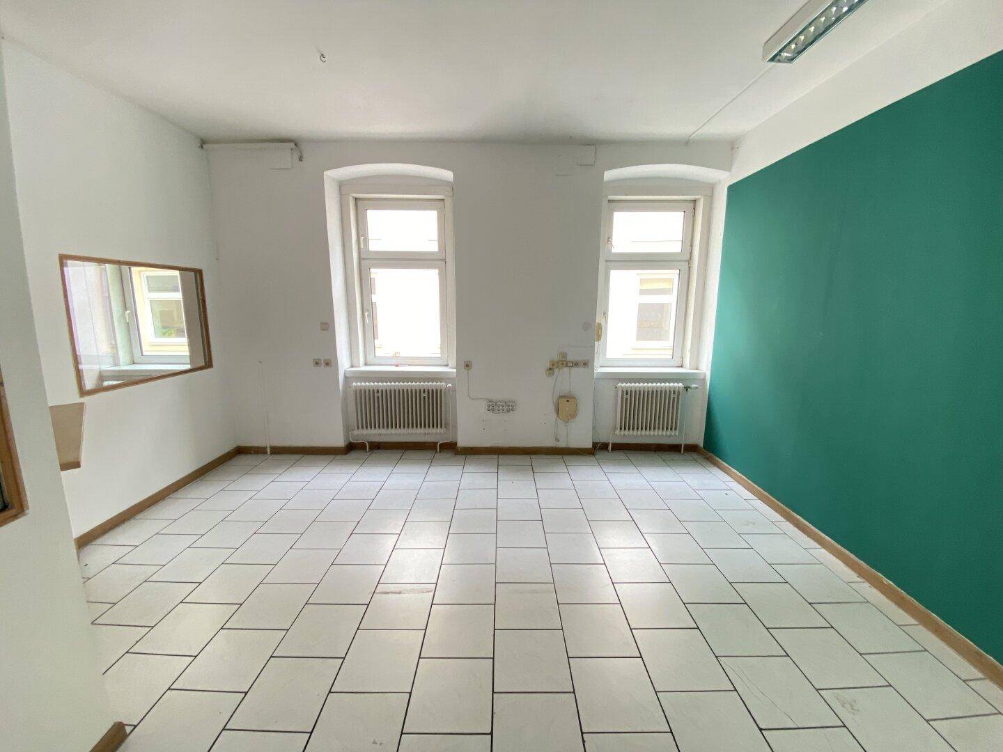 Geräumiger Büroraum mit weißem Fliesenboden und einer auffälligen tealgrünen Akzentwand.