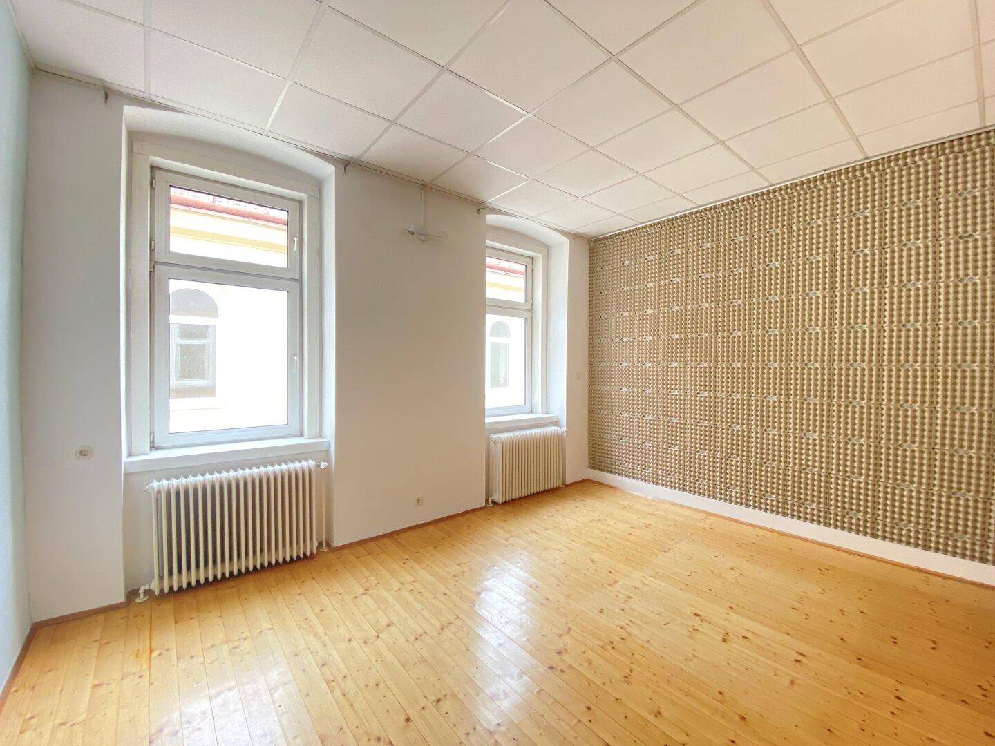 Heller Büroraum mit Holzplankenboden, Rasterdecke und einer dekorativen Tapetenwand, gut beleuchtet.