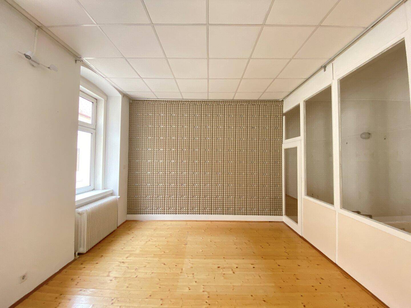 Büroraum mit Holzplankenboden, gemusterter Tapetenwand und Glasabtrennungen, bietet flexible Nutzungsmöglichkeiten.