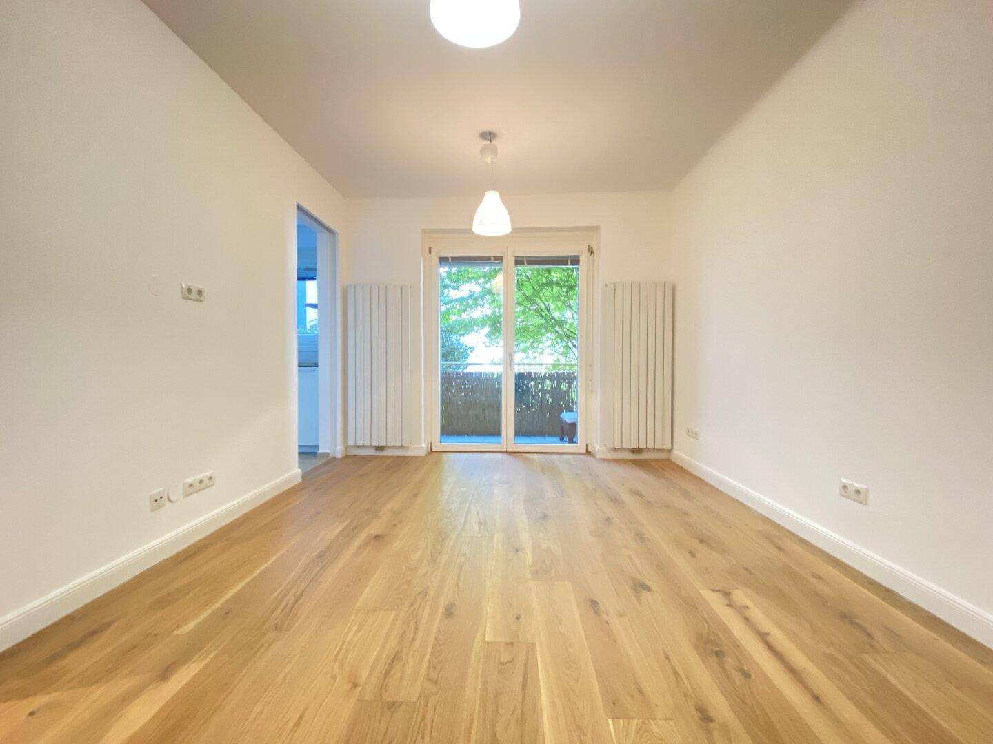 Geräumiges Wohnzimmer mit hellem Parkettboden und großen Fenstern zum Außenbereich.