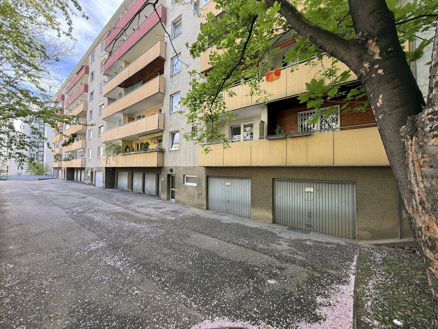 Mehrfamilienhaus mit zahlreichen Balkonen und Garagen im Erdgeschoss, umgeben von Bäumen.