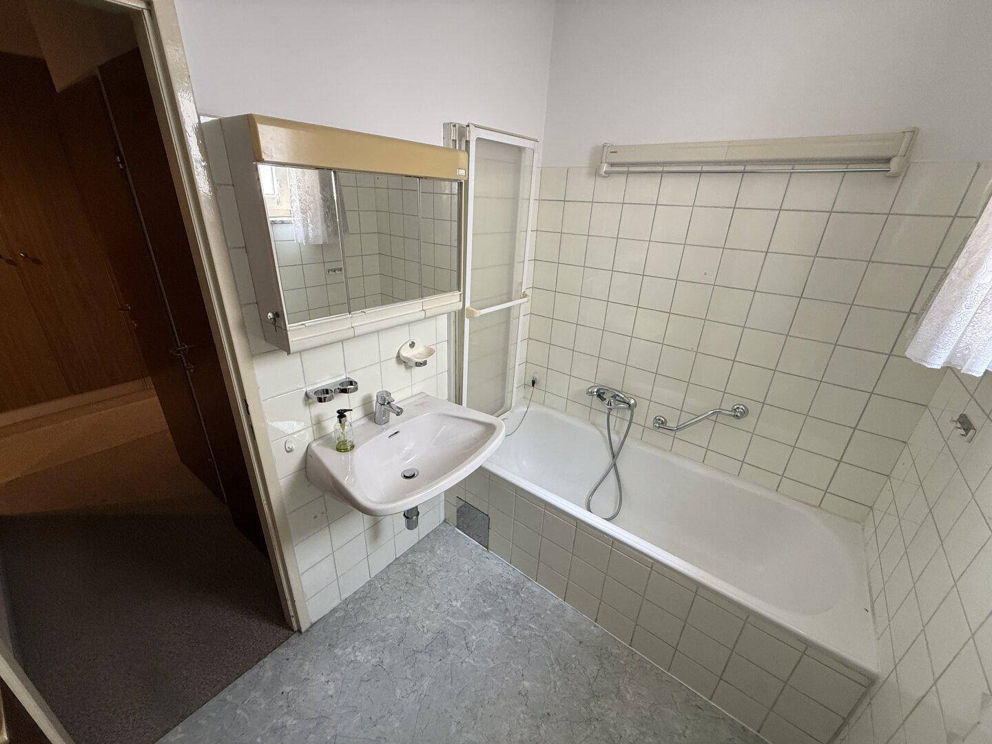 Badezimmer mit Badewanne, Waschbecken und weiß gefliesten Wänden, im Stil der 80er Jahre.