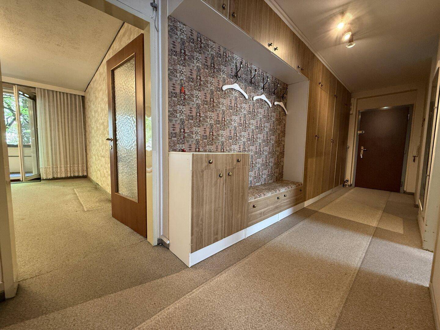 Eingangsbereich mit integrierter Garderobe, Sitzbank und Teppichboden, der zu weiteren Räumen führt.