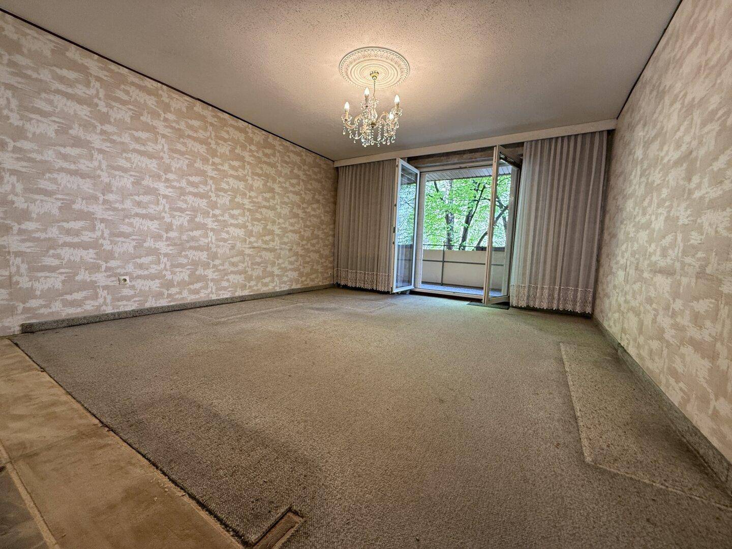 Geräumiges Wohnzimmer mit Teppichboden, Kronleuchter und direktem Zugang zu einem Balkon.