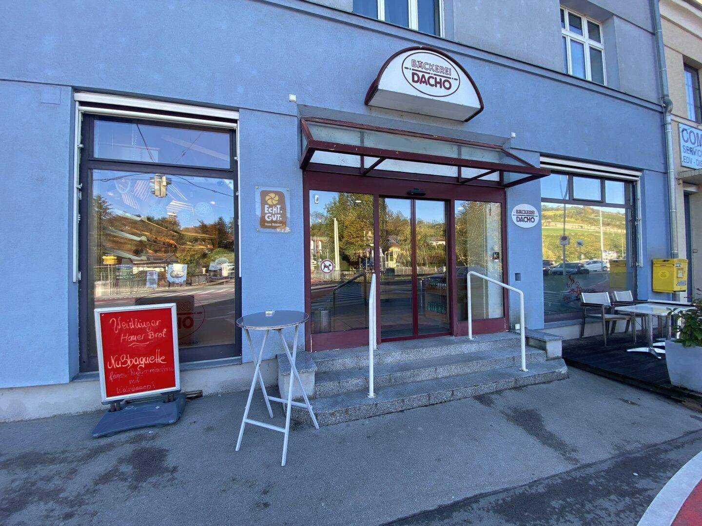 Eingangsbereich der Bäckerei mit Glasfront, Markise und kleinem Außenbereich.