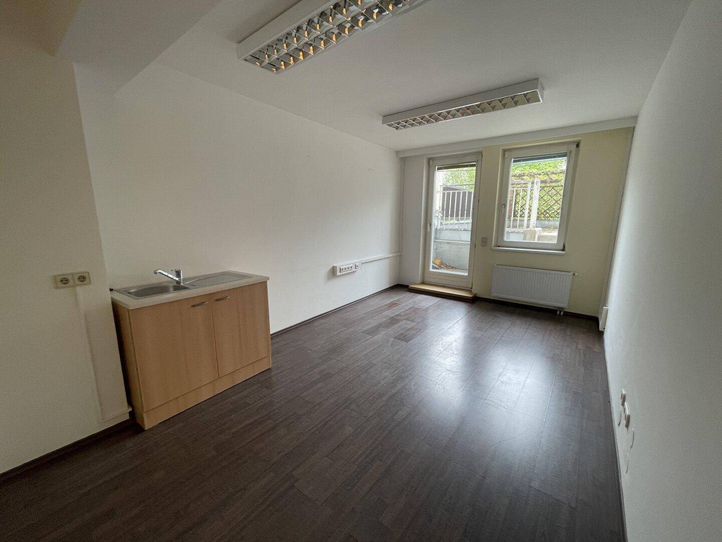 Leerer Raum mit Waschbecken, Fenster und Zugang zu einem Außenbereich, vielseitig nutzbar.