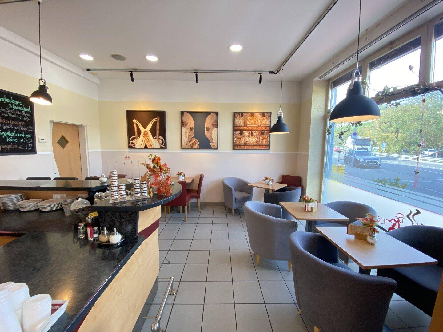 Sitzbereich im Café mit Kunstwerken an der Wand, dunkler Theke und hellen Fliesen.