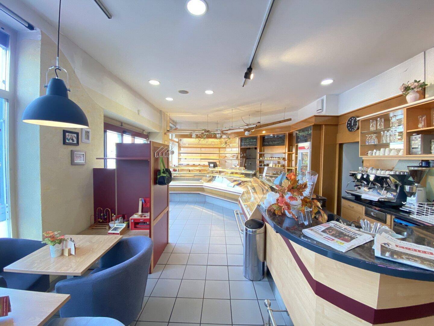 Übersicht des Bäckerei-Cafés mit Verkaufsbereich, Theke und gemütlichen Sitzgelegenheiten.