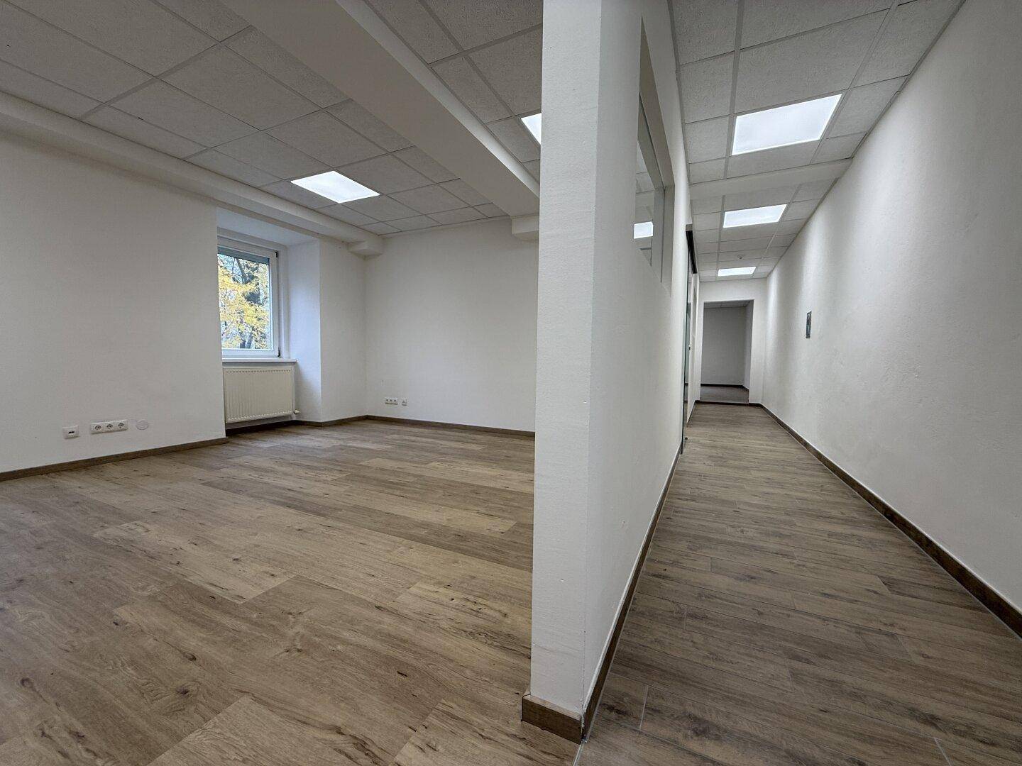 Langer, heller Flur mit Laminatboden und Deckenbeleuchtung, der zu weiteren Büroräumen führt.