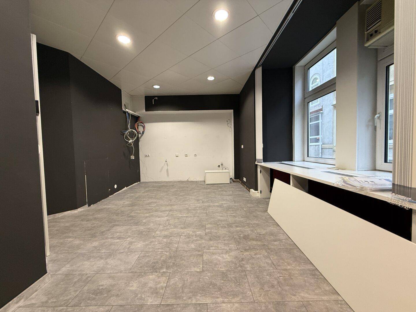 Geräumiger Büroraum mit dunklen Wänden, Fliesenboden und sichtbaren Installationen, bereit zur Gestaltung.