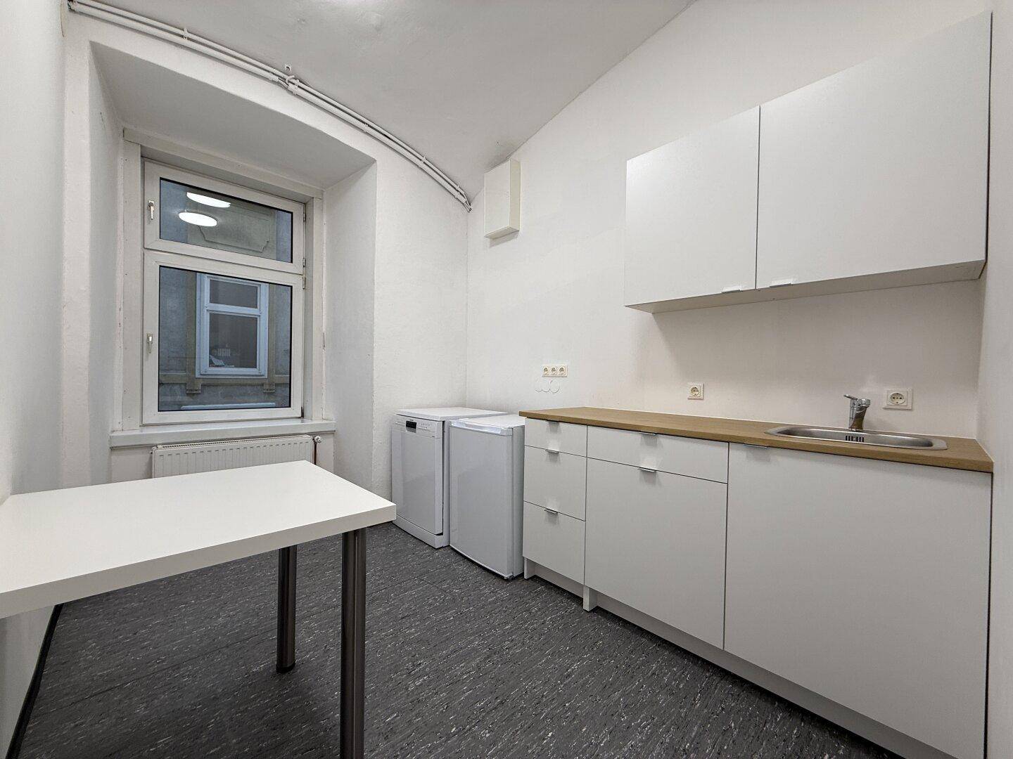 Kleine Küchenzeile mit weißen Schränken, Holzarbeitsplatte und Fenster, inklusive Spülmaschine und Kühlschrank.