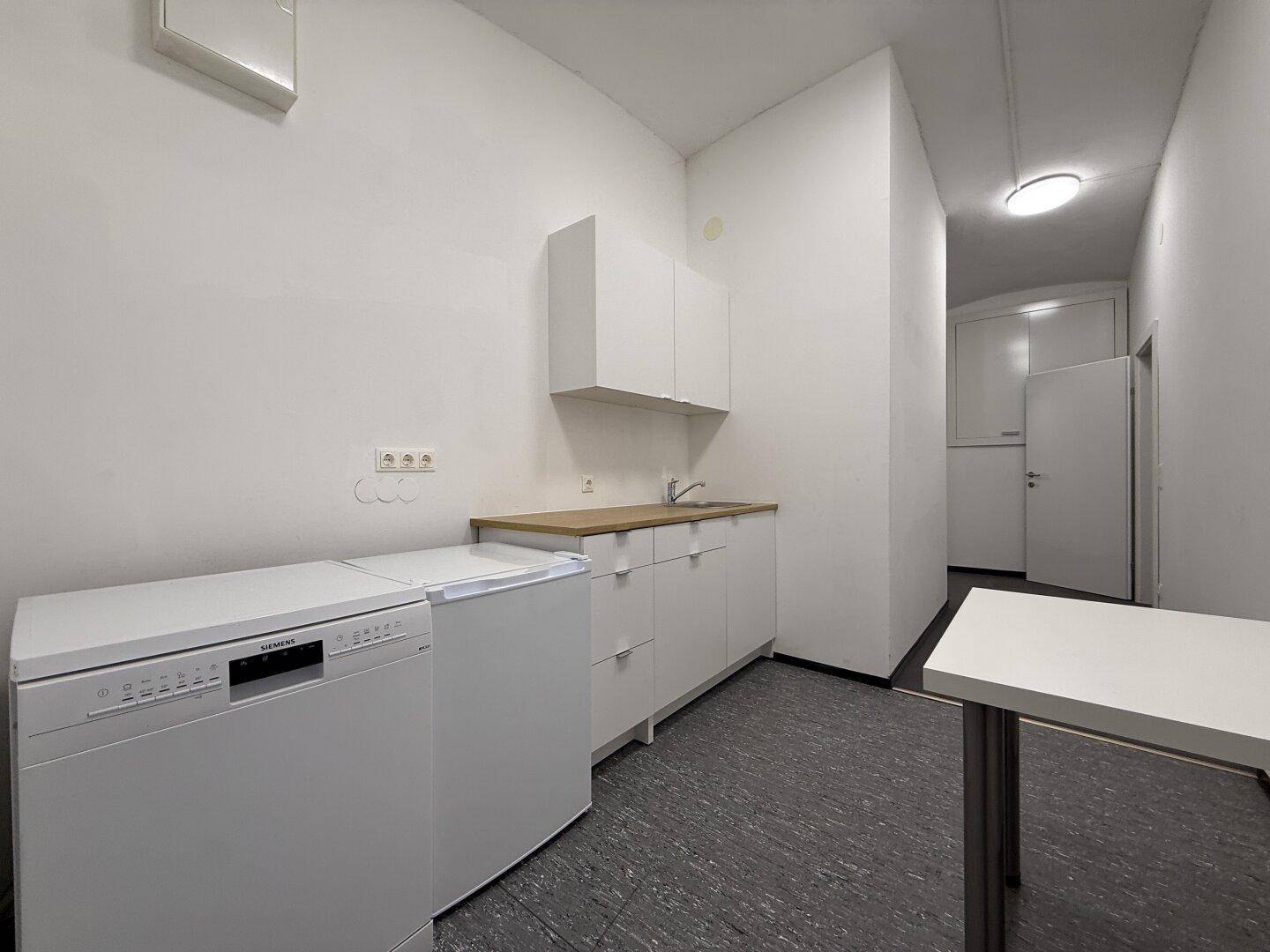 Funktionale Küchenzeile mit weißen Schränken, Spülmaschine und Kühlschrank, ideal für kleine Büros.