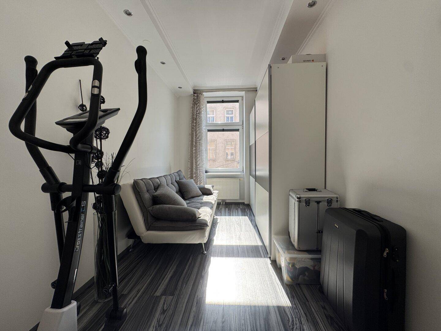 Schmaler Raum mit Sofa, Fitnessgerät und Stauraum, ideal als Gäste- oder Arbeitszimmer.
