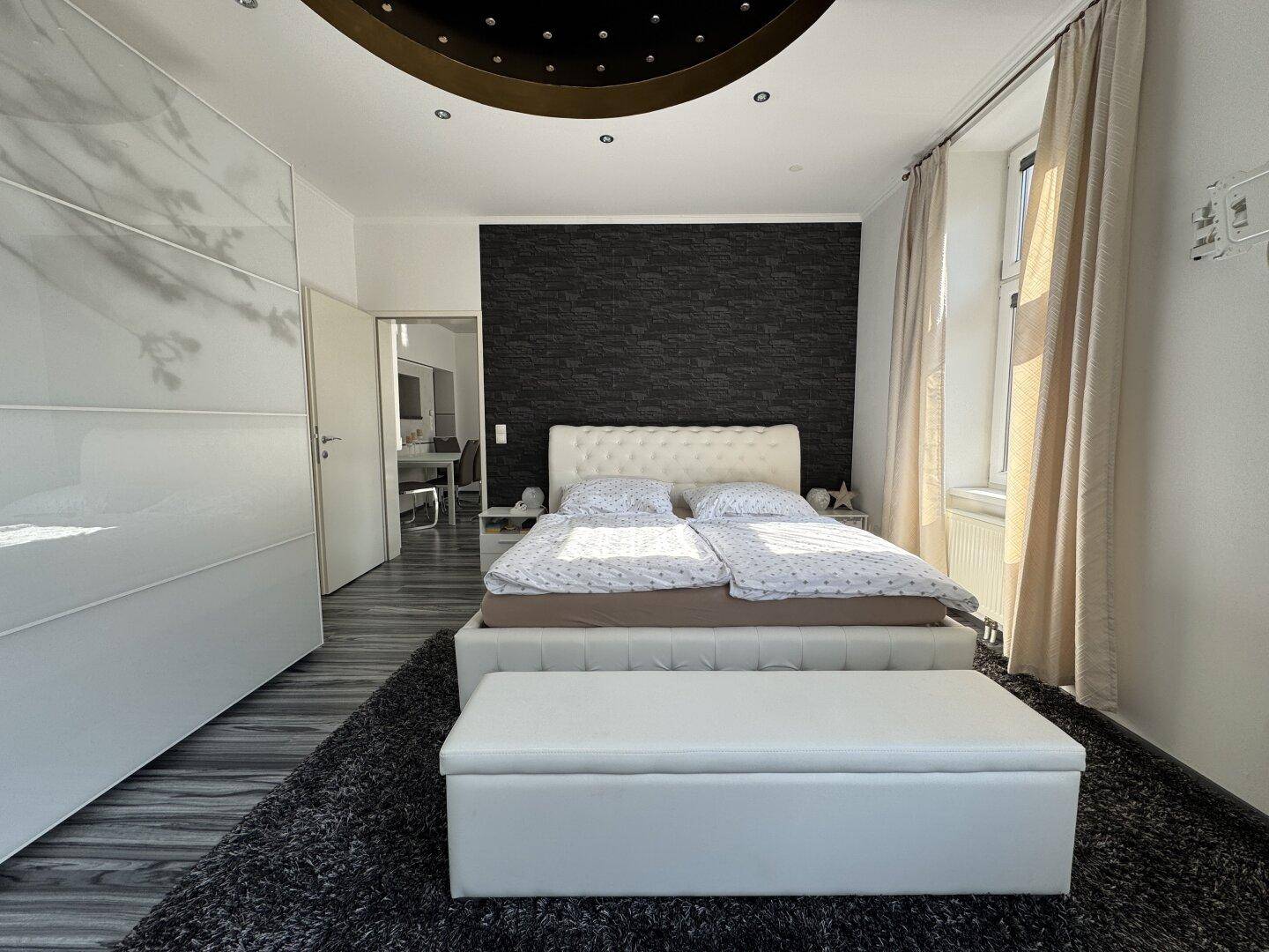 Gemütliches Schlafzimmer mit weißem Doppelbett, dunkler Akzentwand und großem Kleiderschrank.