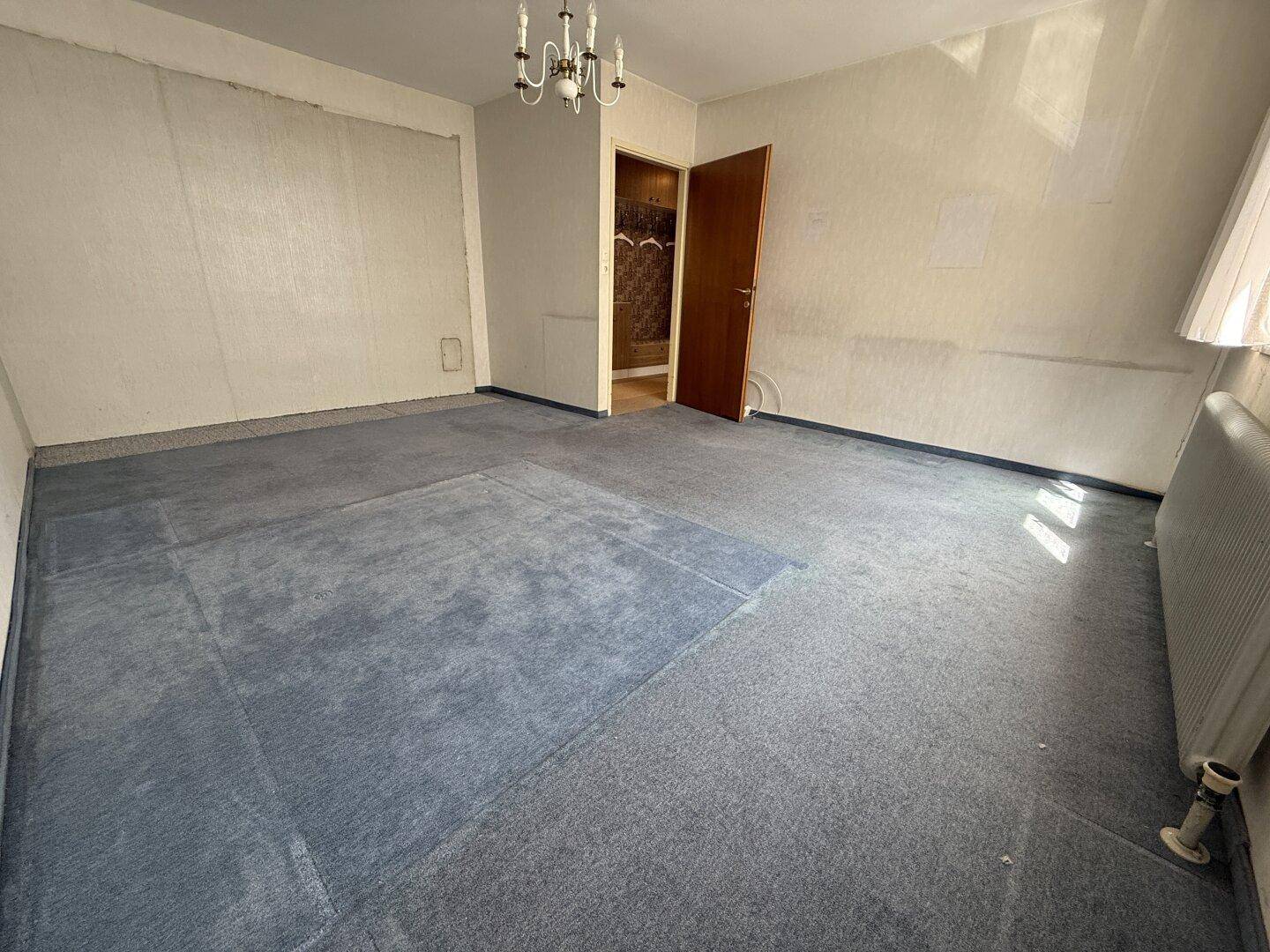 Leerer Raum mit abgenutztem blauem Teppichboden und Tür, die zu einem weiteren Bereich führt.