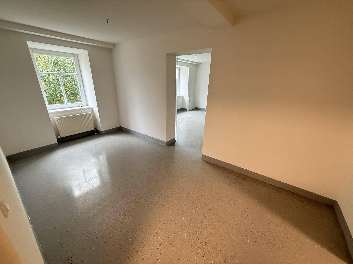 Geräumiger, heller Raum mit einem Fenster, das viel Tageslicht hereinlässt, und glänzendem Bodenbelag.