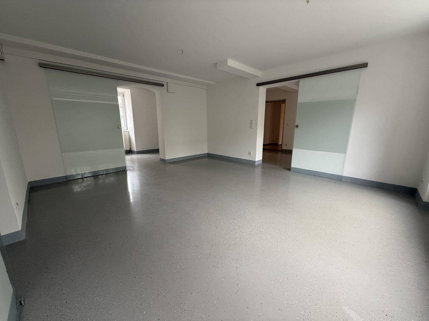 Großer, offener Raum mit glänzendem Boden und zwei Glasschiebetüren, die zu weiteren Zimmern führen.