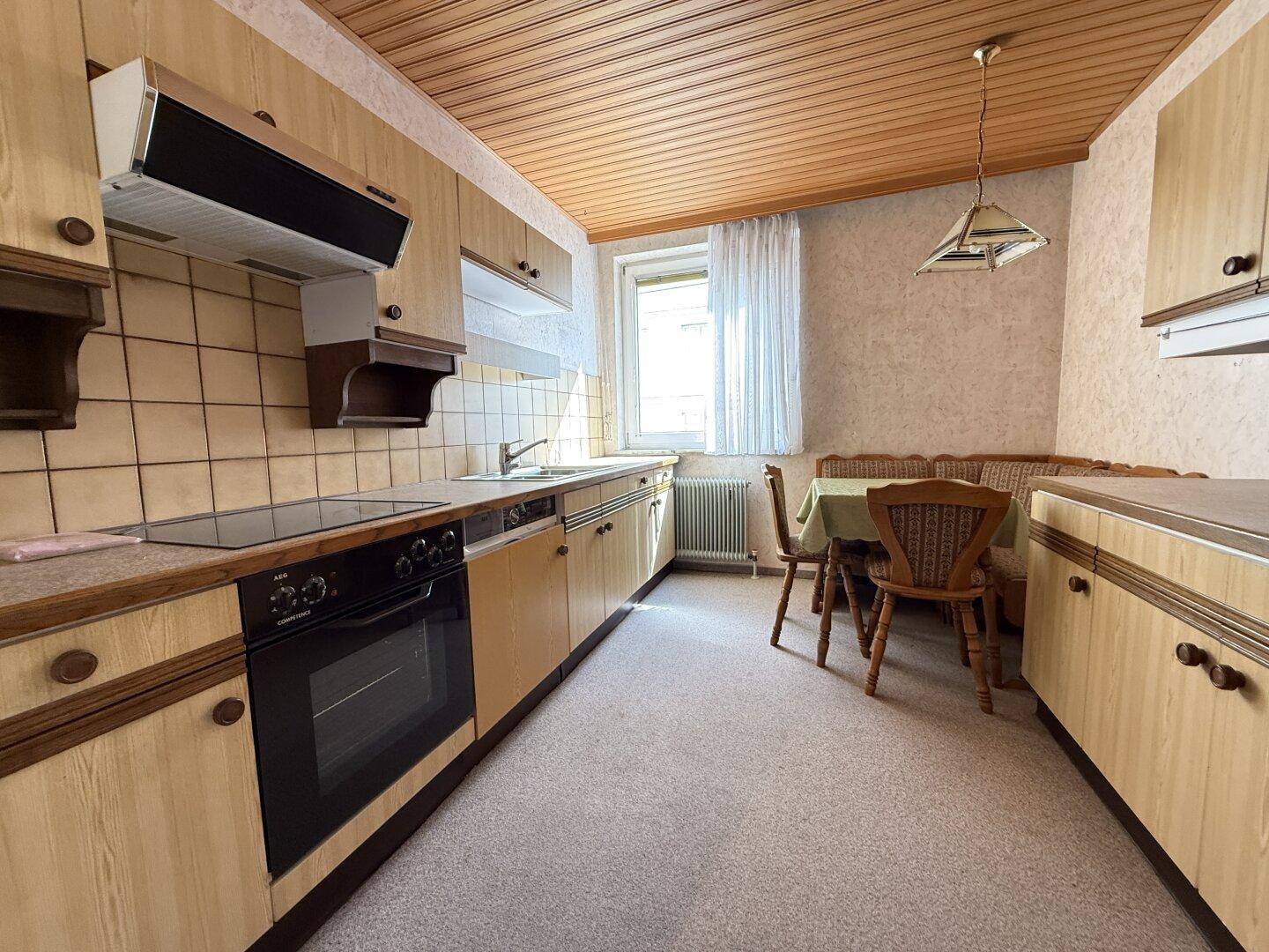 Gemütliche Wohnküche mit Holzschränken, Einbaugeräten und einem Essbereich mit Bank und Tisch.