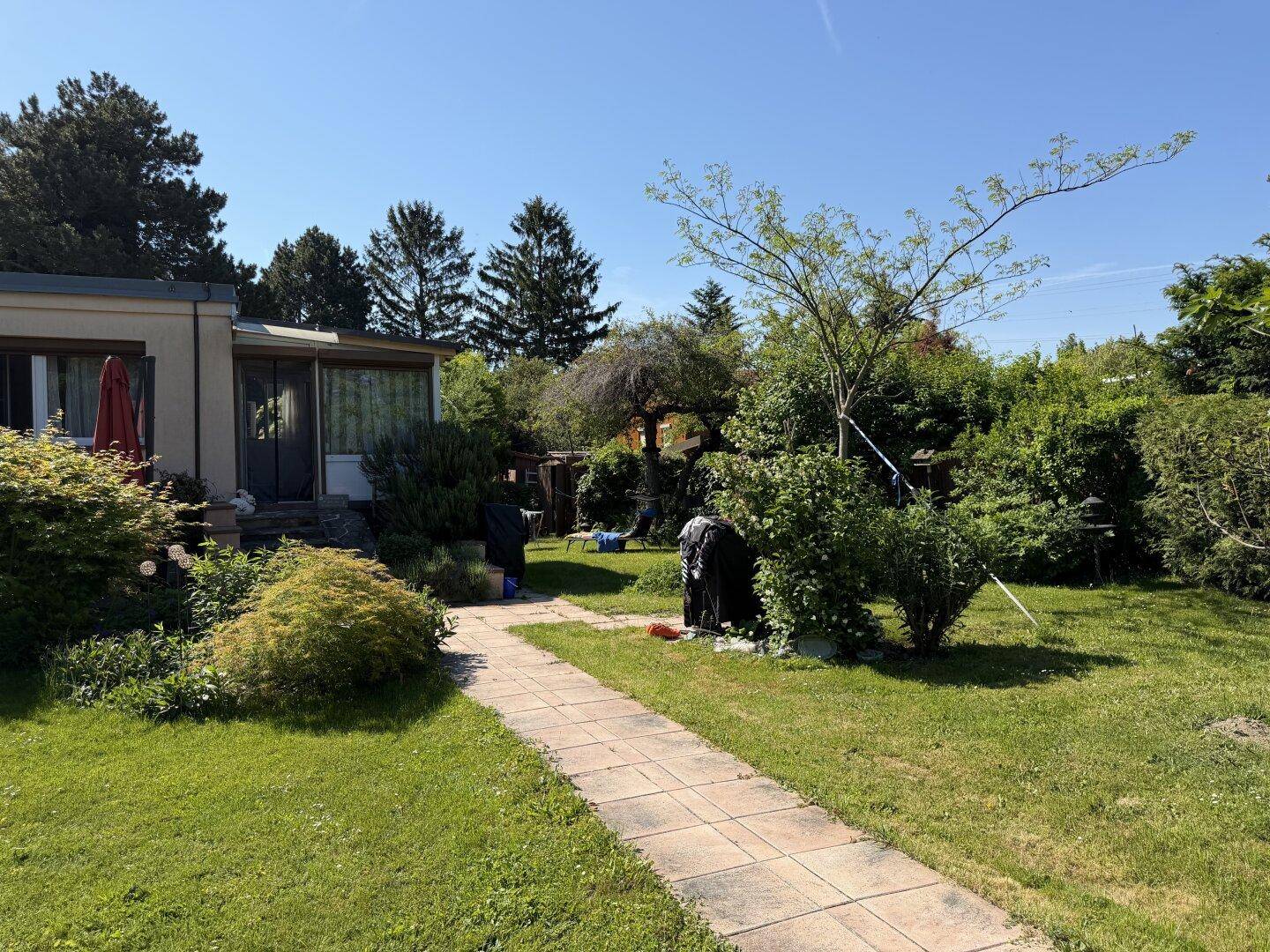 Weitläufiger Garten mit Rasenfläche, gepflastertem Weg und üppiger Bepflanzung neben dem Haus.