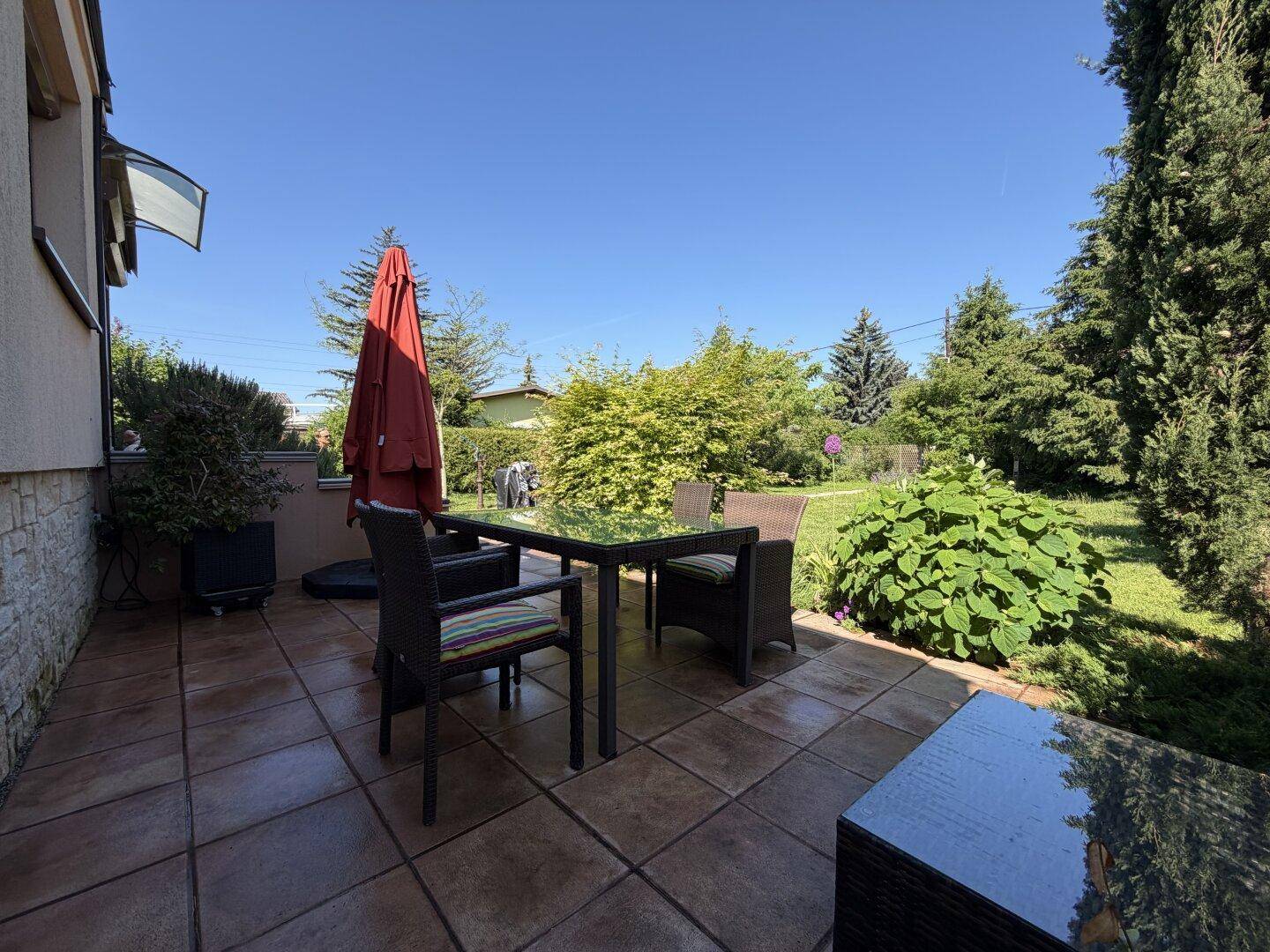Gemütliche geflieste Terrasse mit Gartenmöbeln, Sonnenschirm und Blick ins Grüne.