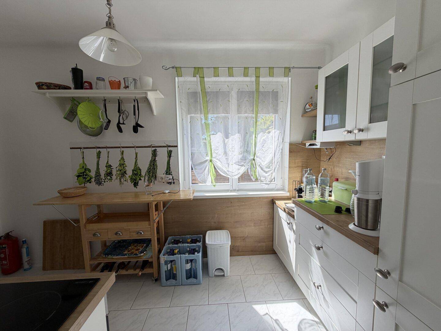 Funktionale Küche mit weißen Fronten, Holzdetails und einem Fenster mit Blick ins Freie.