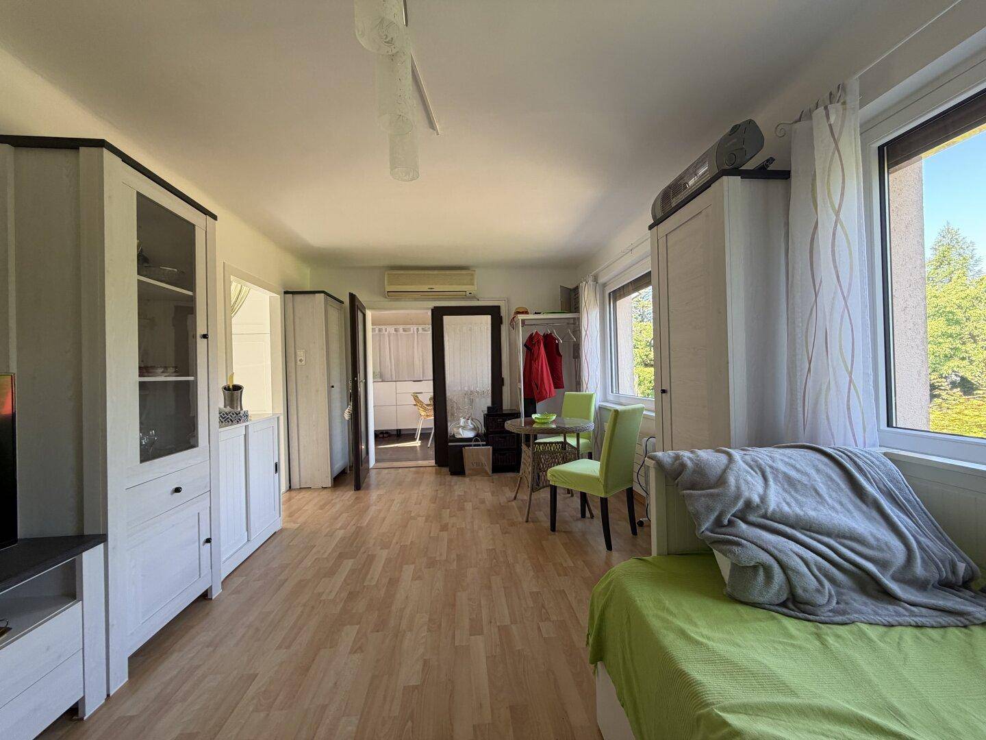Geräumiges Wohnzimmer mit Laminatboden, Blick in die Küche und einfacher Möblierung.