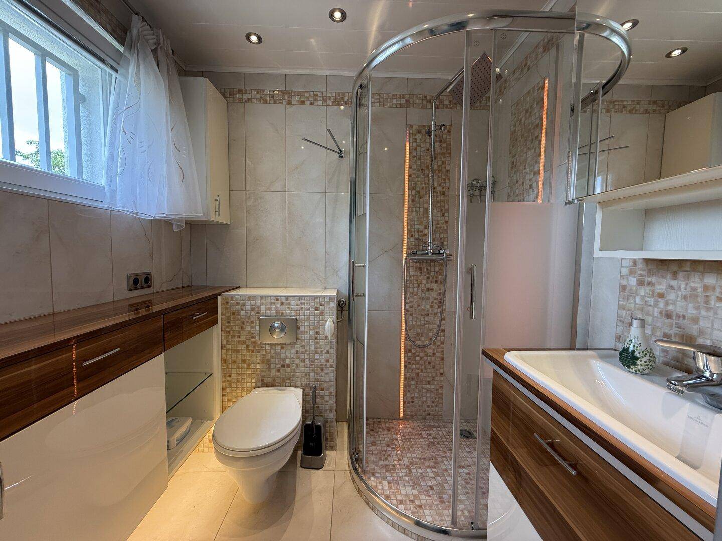 Modernes Badezimmer mit Eckdusche, WC, Einzelwaschbecken und Fenster für Tageslicht.