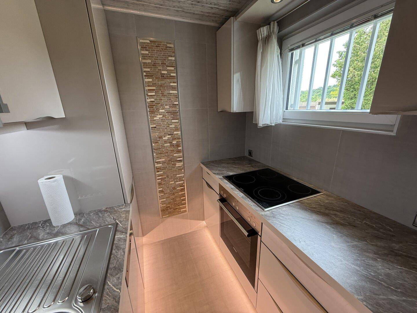 Funktionale Küche mit Induktionskochfeld, Backofen und Fenster, ausgestattet mit modernen Fliesen.