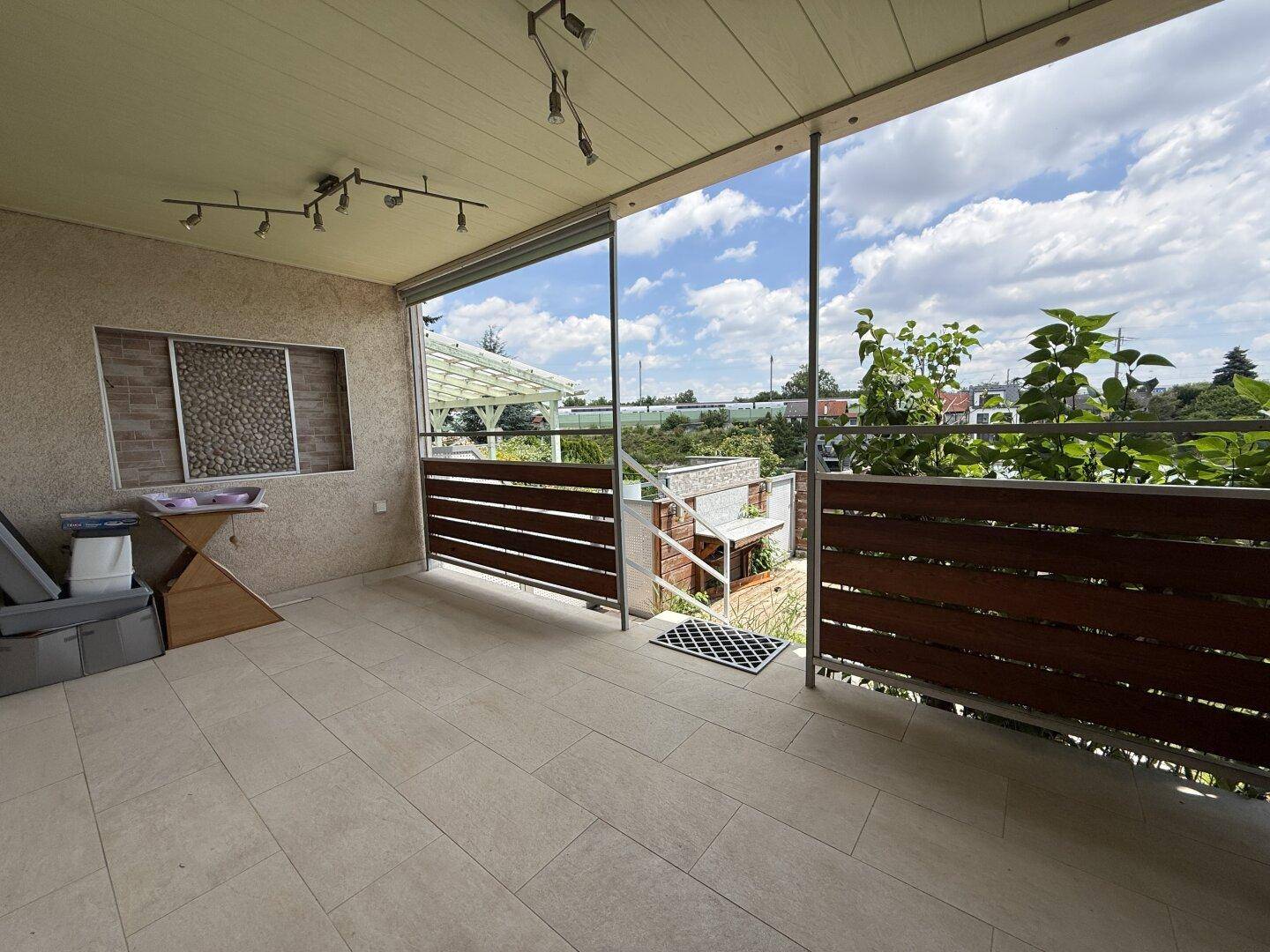 Überdachte Terrasse mit Fliesenboden und Holzelementen, bietet einen Blick ins Grüne.