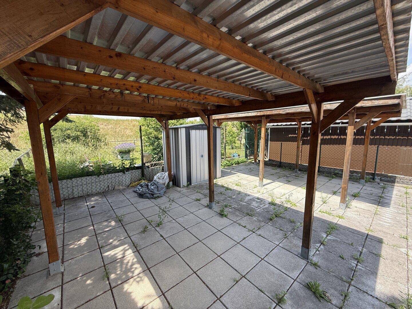 Überdachter Parkplatz unter einem Holz-Carport mit gepflastertem Boden.