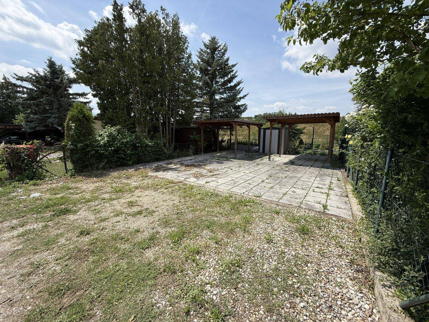Außenbereich mit gepflasterter Fläche, Kies und zwei Holz-Carports.