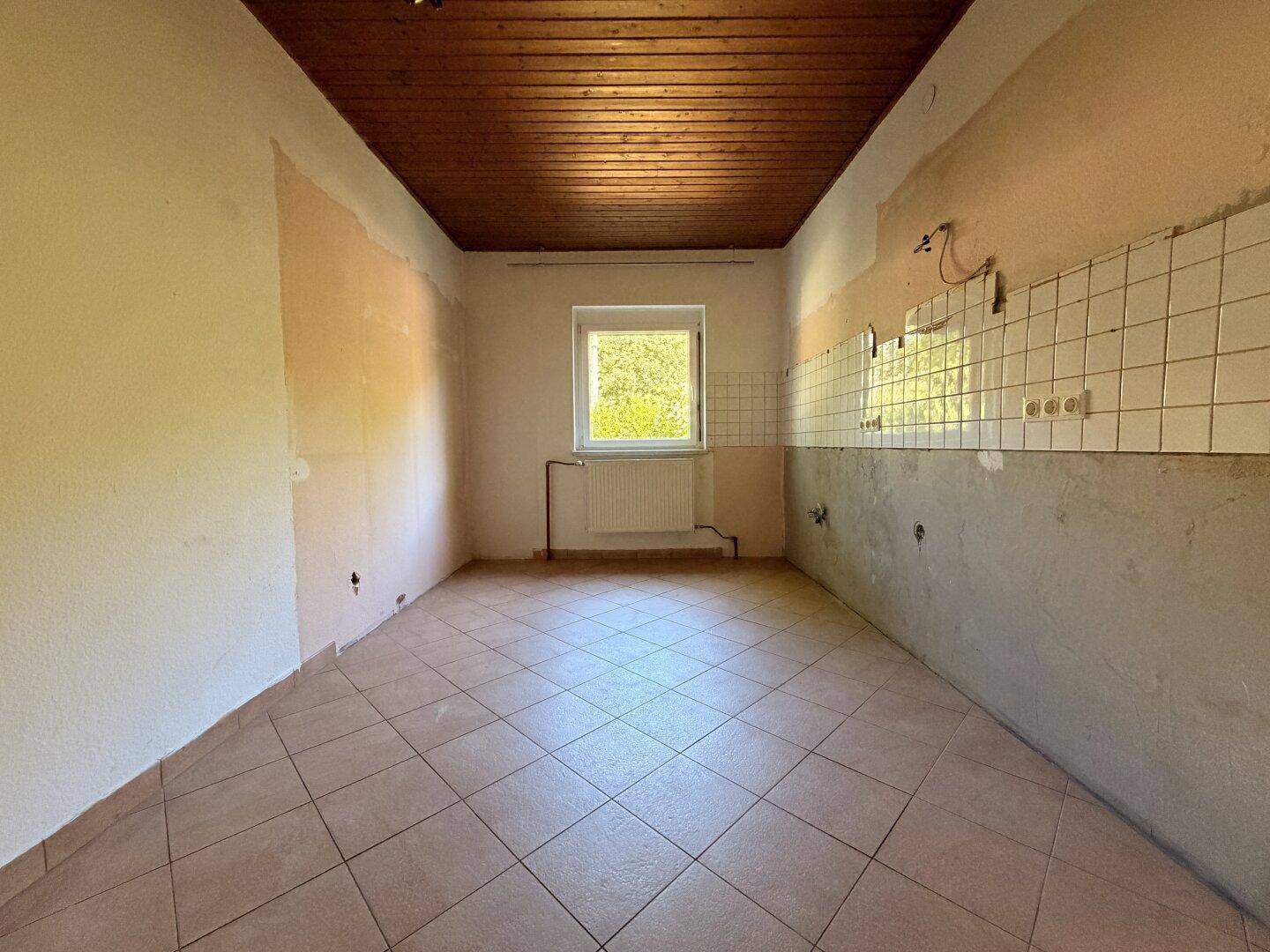 Leerer Küchenraum mit Fliesenboden und Fenster, bereit für eine neue Kücheninstallation.