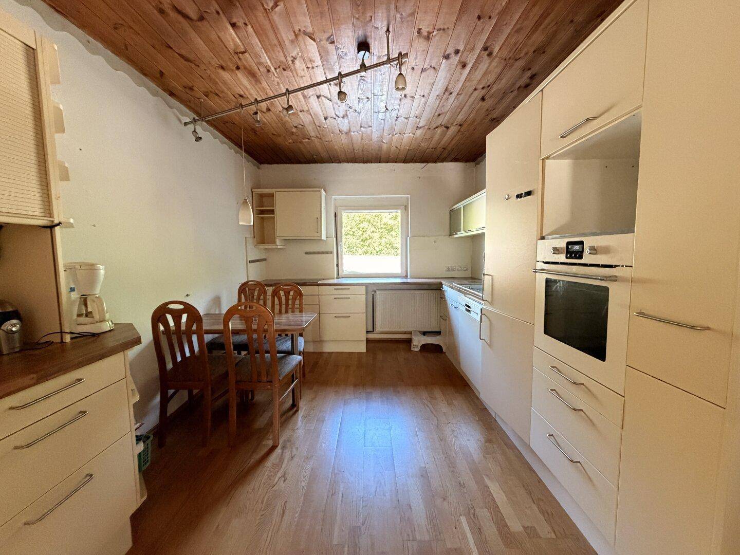 Funktionale Küche mit Holzbalkendecke, Einbauschränken und einem Essbereich am Fenster.