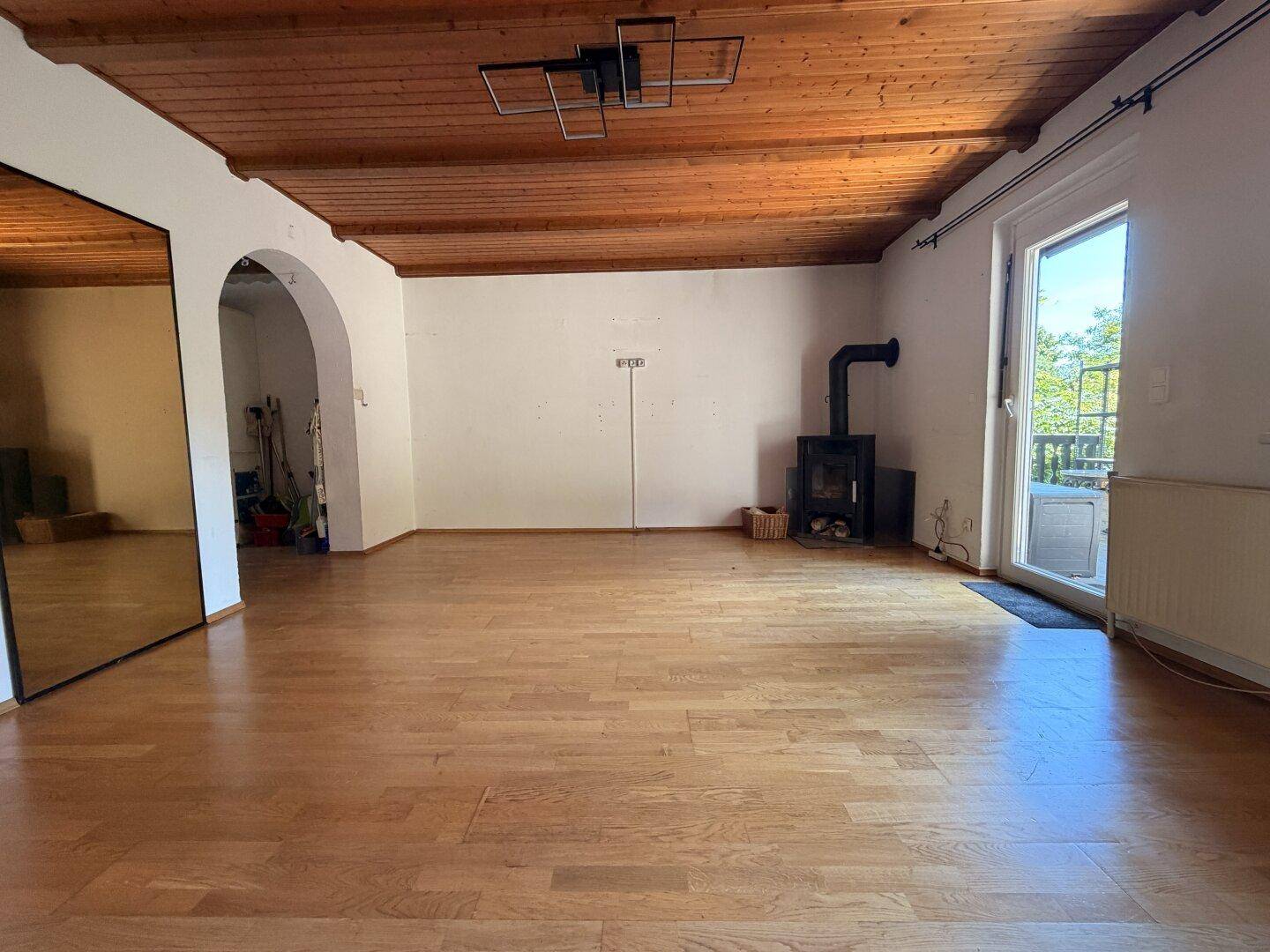 Geräumiges Wohnzimmer mit Holzbalkendecke, Parkettboden, Holzofen und großem Wandspiegel.