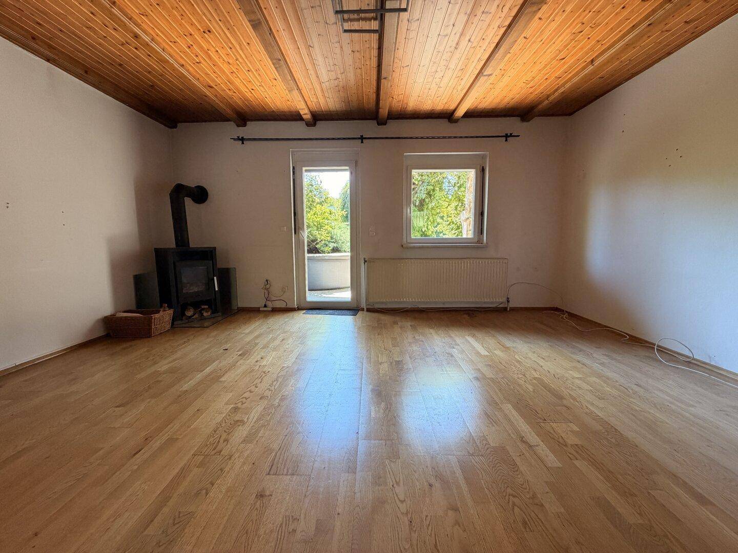 Helles Wohnzimmer mit Holzbalkendecke, Parkettboden und einem modernen Holzofen.
