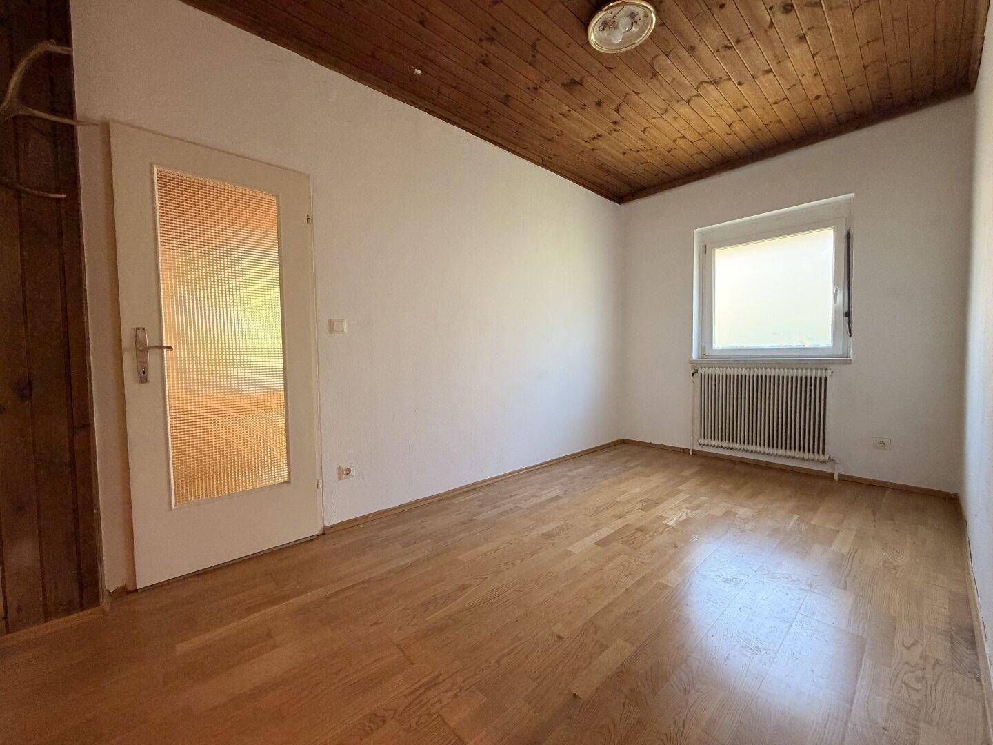 Gemütliches Zimmer mit Holzbalkendecke, Parkettboden und einer Tür mit Glaseinsatz.