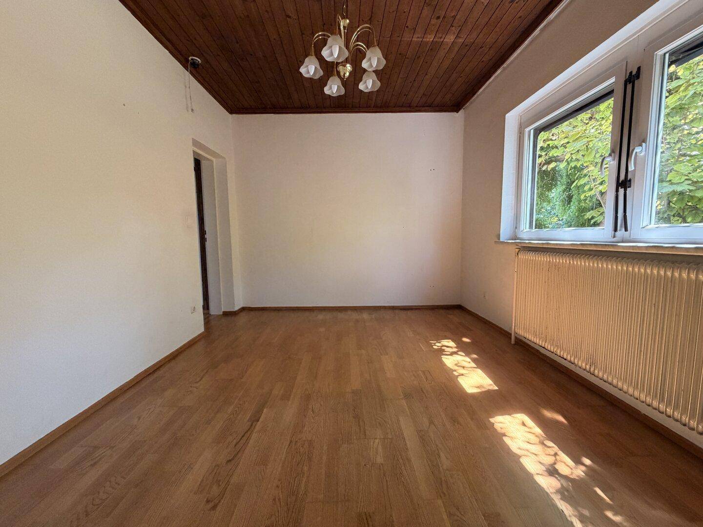 Geräumiges Zimmer mit Holzbalkendecke, Parkettboden und viel Tageslicht durch das große Fenster.