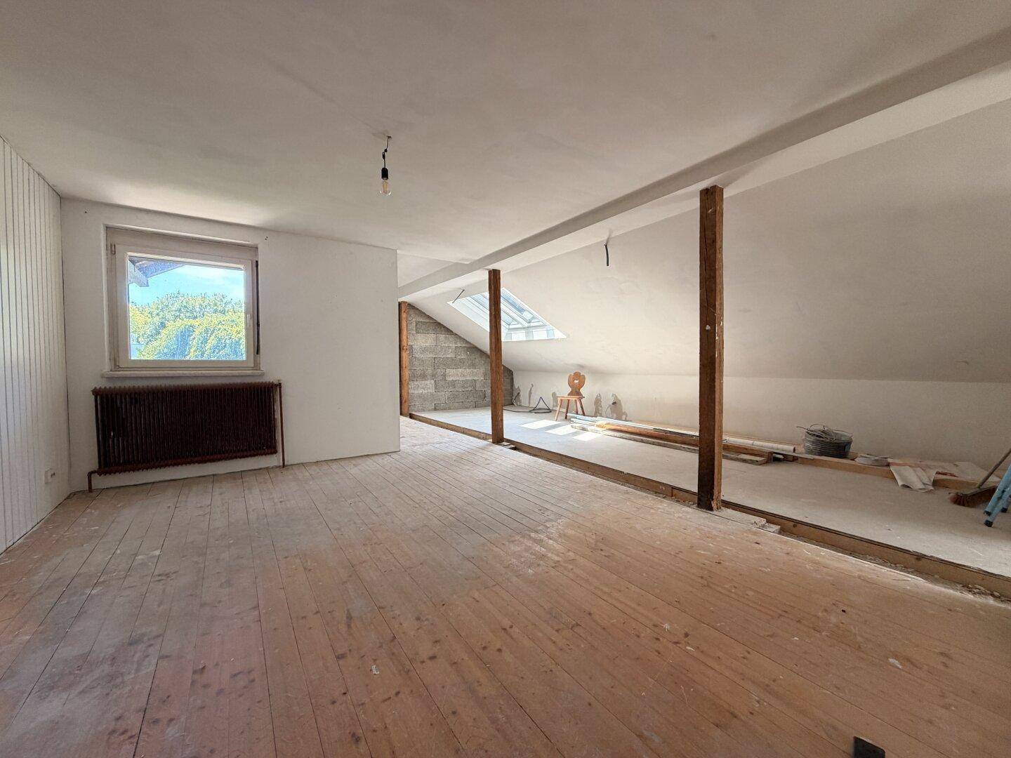 Ausbaufähiger Dachbodenbereich mit Holzboden, Dachfenster und sichtbaren Holzbalken.