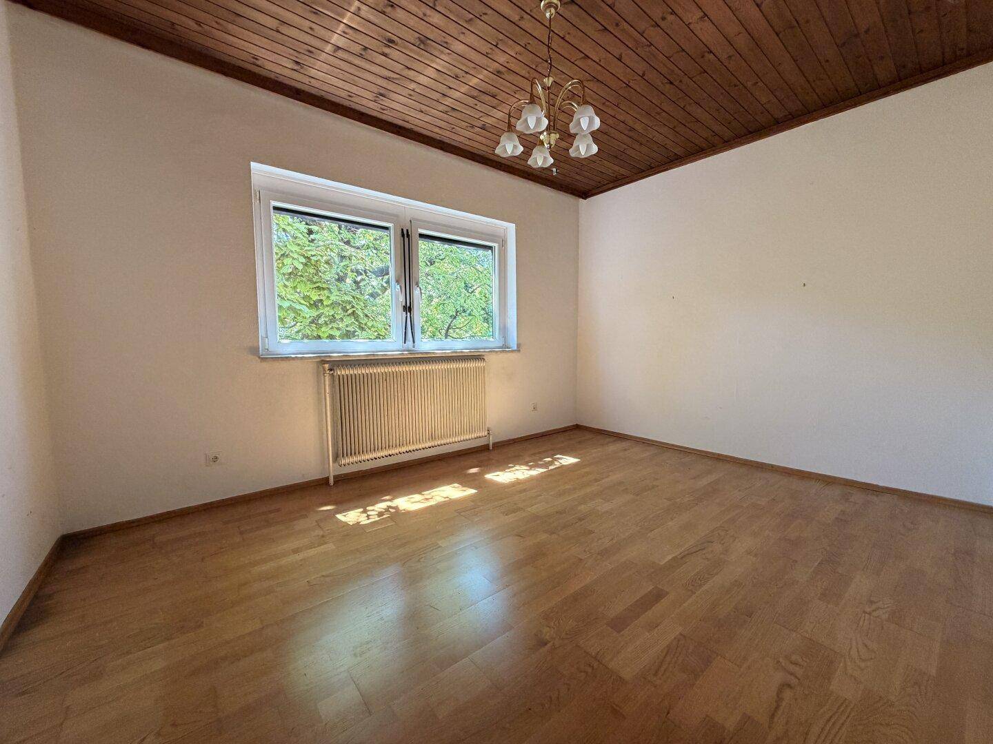 Helles Zimmer mit Holzbalkendecke, Parkettboden und einem Kronleuchter, ideal als Schlafzimmer.