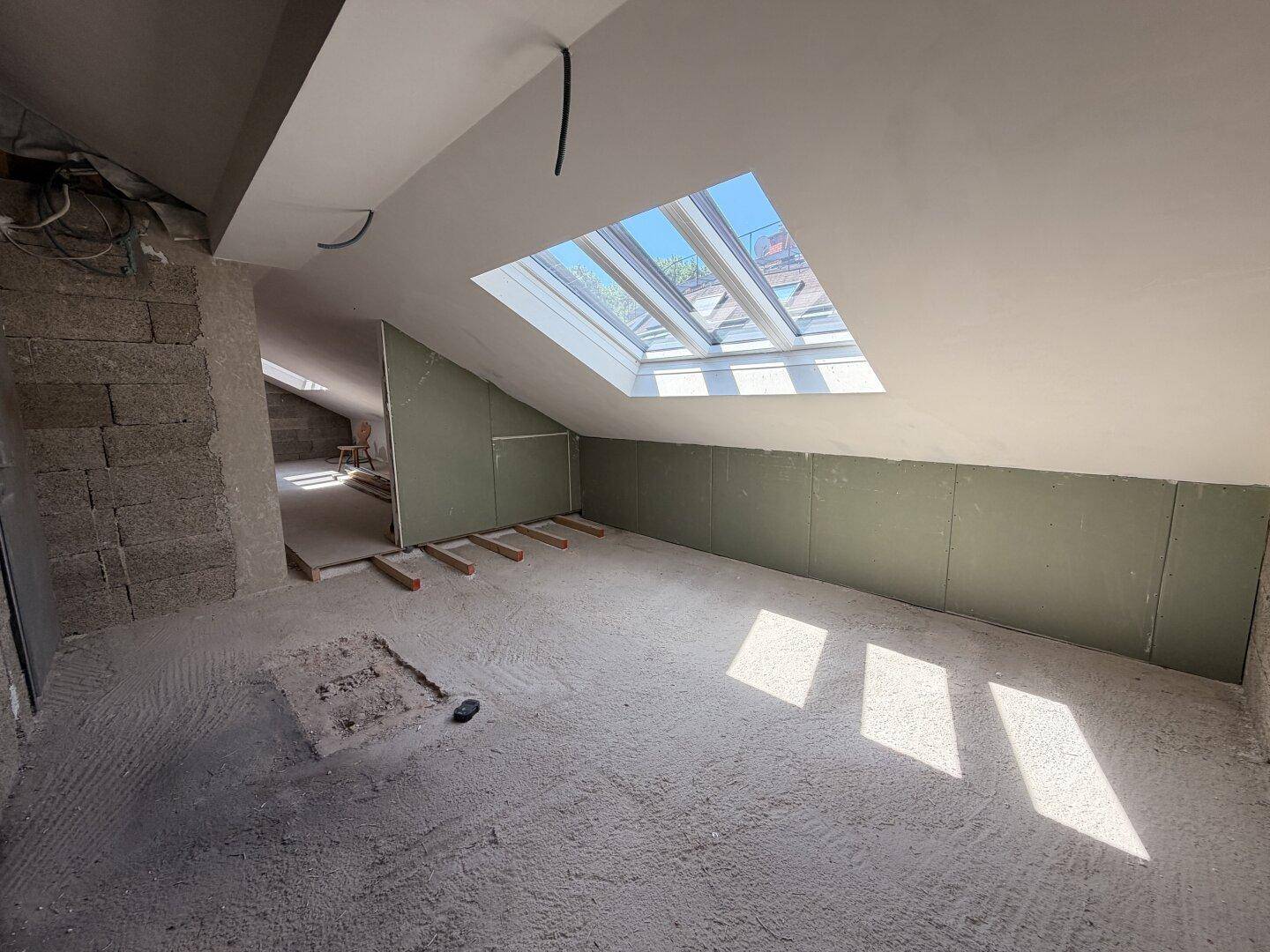 Dachbodenbereich mit Dachfenster und vorbereiteten Wänden für den Innenausbau.