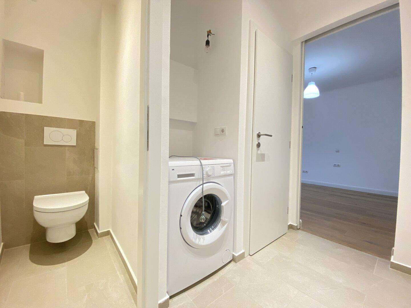 Praktischer Bereich mit Wand-WC und integrierter Waschmaschine in hellem Design.