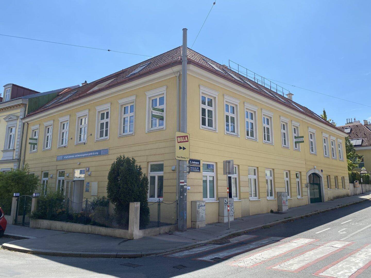 Gelbes Eckgebäude mit traditioneller Architektur und vielen Fenstern an einem sonnigen Tag.