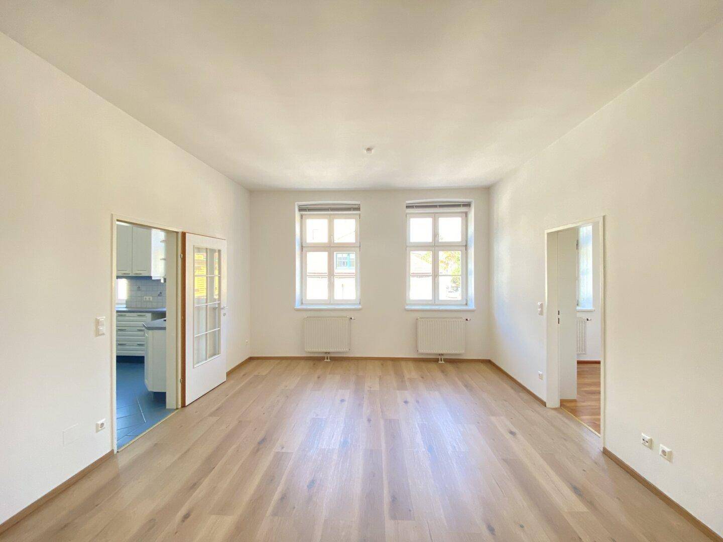 Helles, leeres Wohnzimmer mit neuem Holzparkettboden und zwei großen Fenstern.