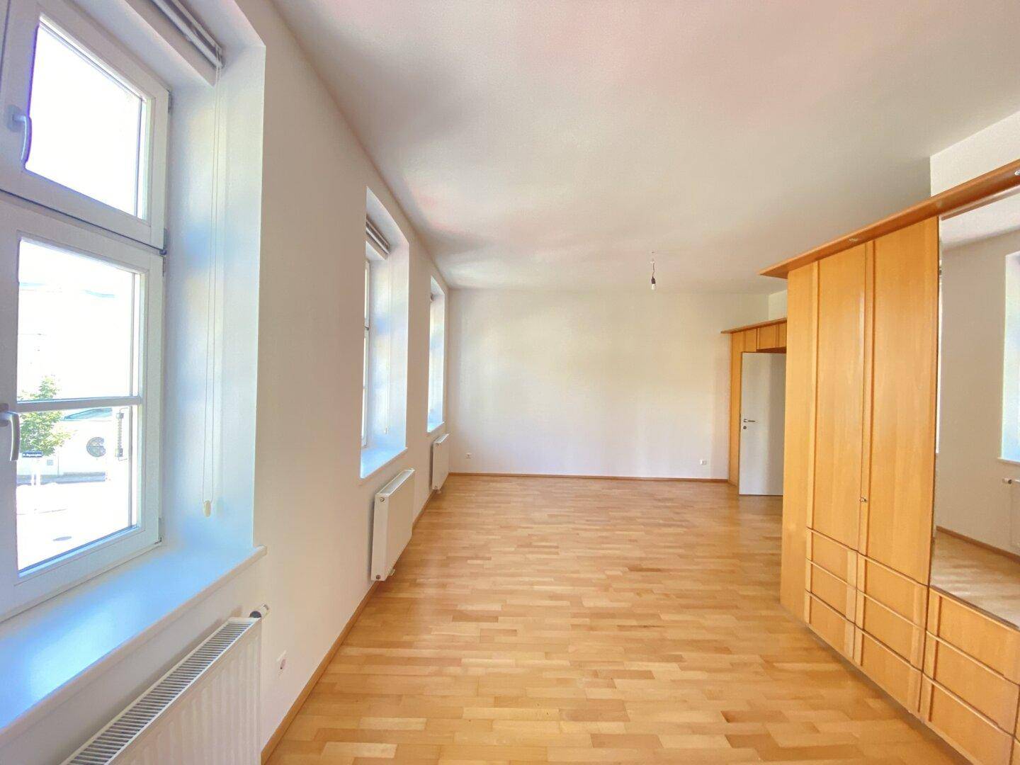 Weitläufiges Schlafzimmer mit hellem Holzparkett, hohen Decken und viel Tageslicht.