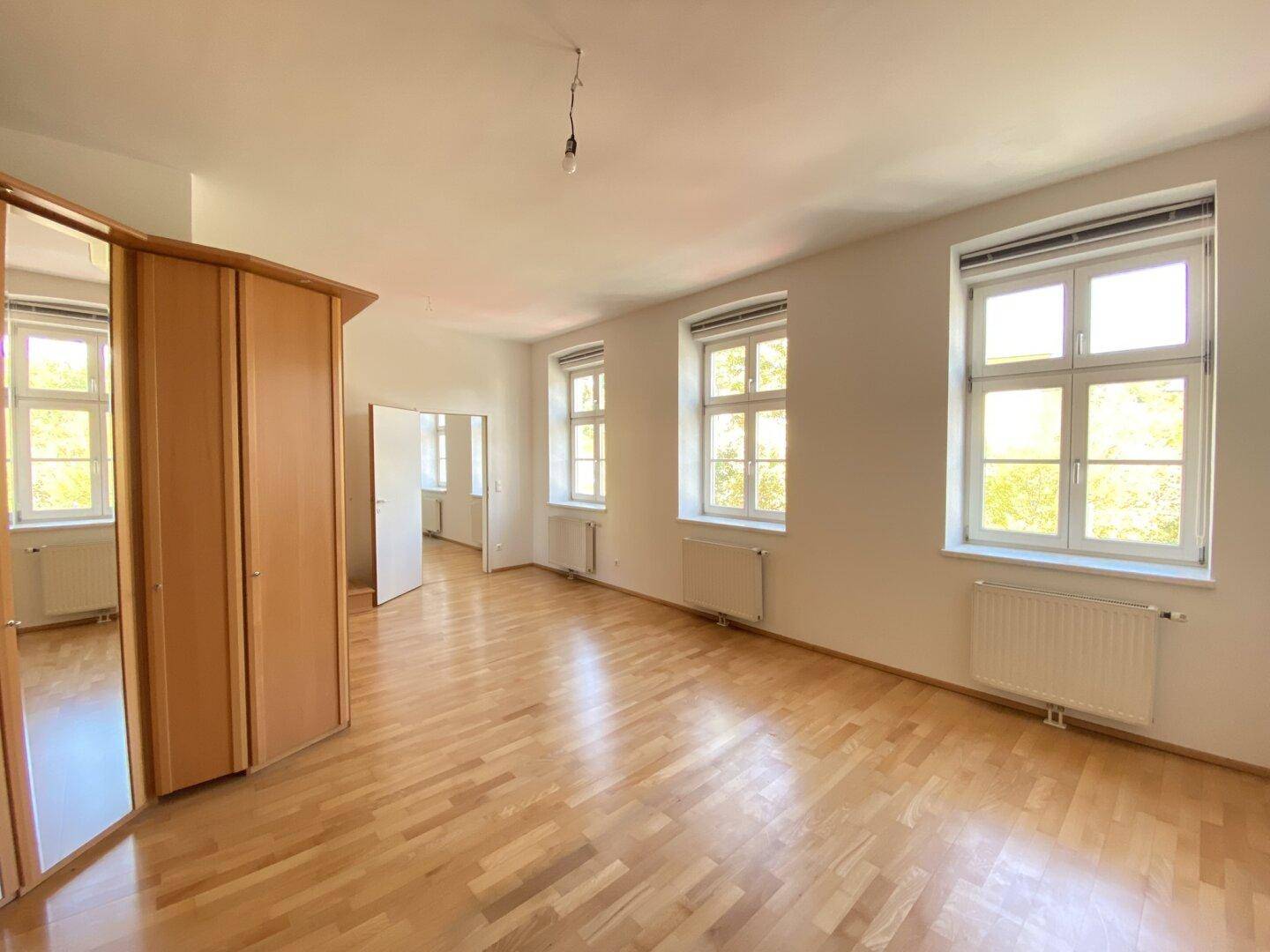 Geräumiges Schlafzimmer mit Holzparkettboden, mehreren Fenstern und einem großen Kleiderschrank.