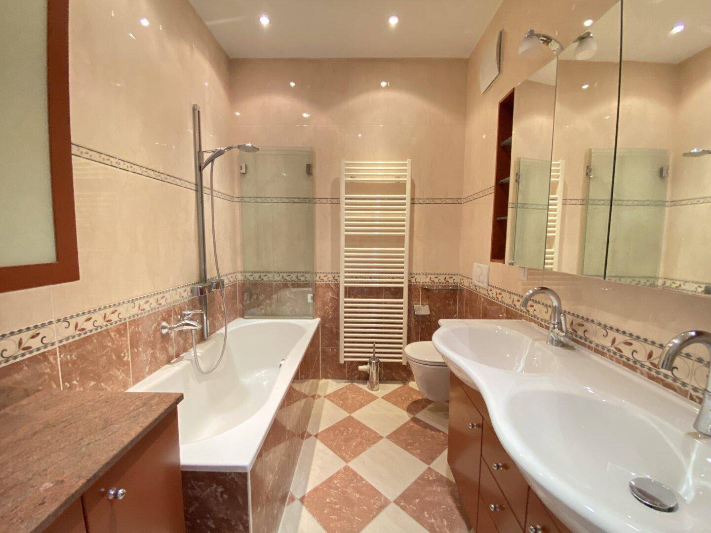 Badezimmer mit Doppelwaschbecken, Badewanne und gemusterten Fliesen in warmen Farbtönen.