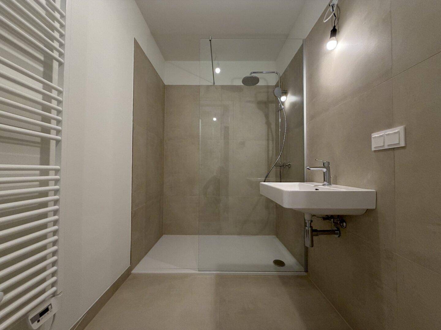 Modernes Badezimmer mit ebenerdiger Dusche, Regenbrause und beheiztem Handtuchhalter.