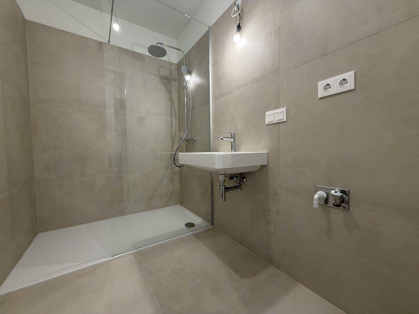 Zeitgemäßes Badezimmer mit großer ebenerdiger Dusche und modernem Waschbecken.